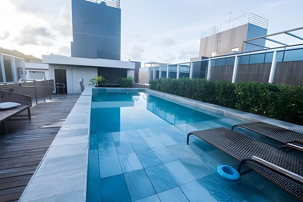 A rooftop pool with a wooden deck, lounge chairs, and a view of modern buildings. - Vivendas do Mar (João Pessoa)