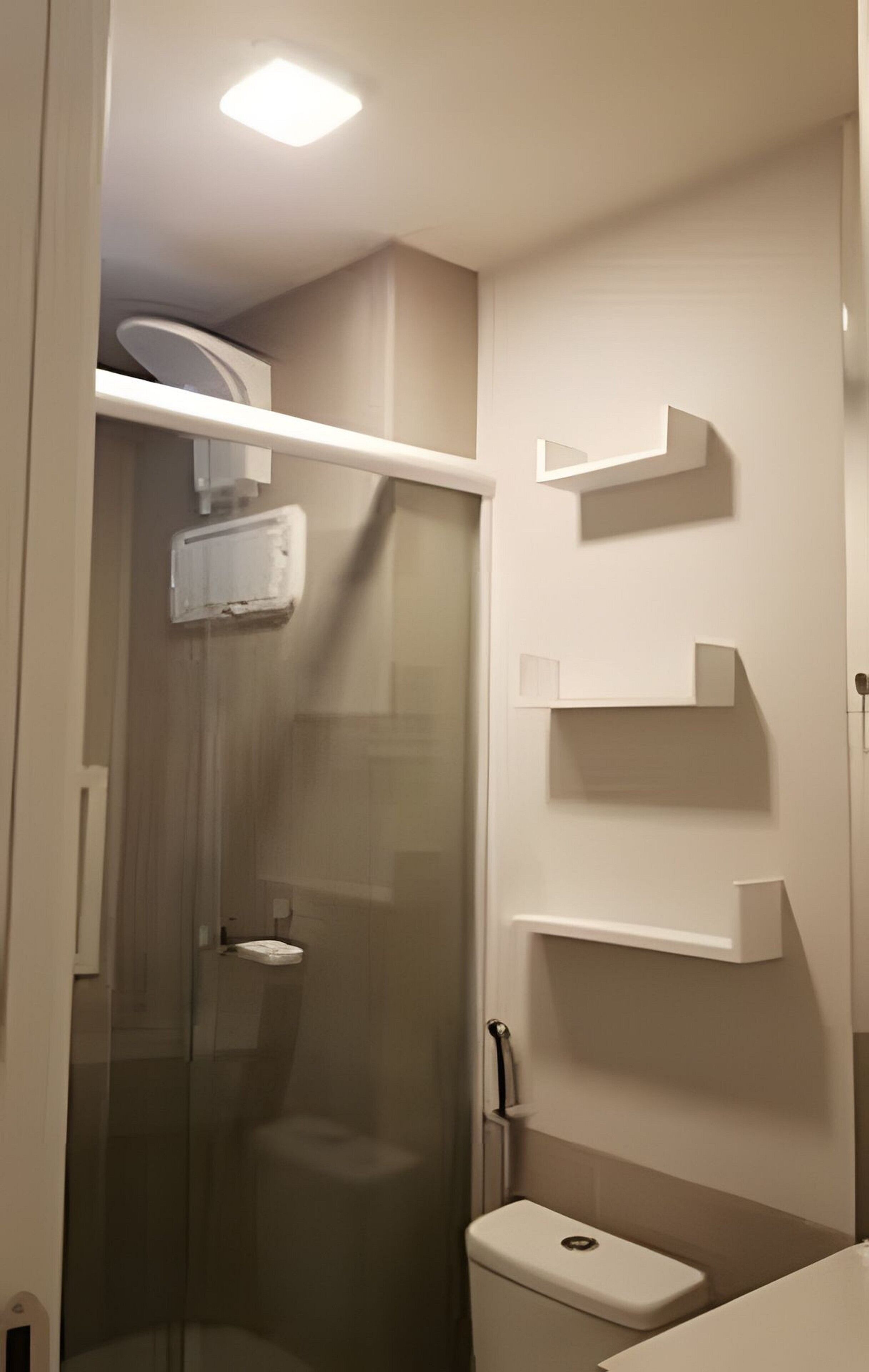 Een badkamer met een douche met glazen wand, een toilet en wandplanken.