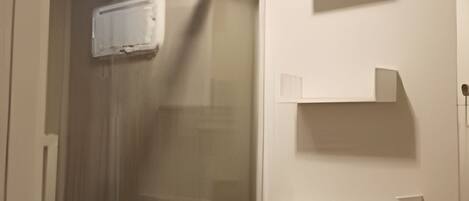 A bathroom with a glass-enclosed shower, a toilet, and wall-mounted storage shelves.