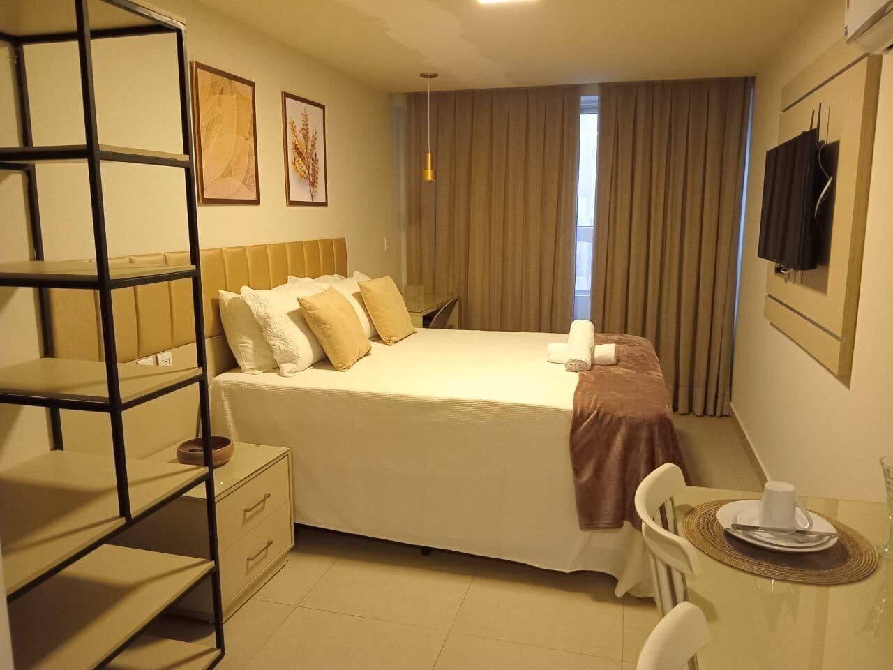 A hotel room with a bed, a desk with a chair, a small table with a cup and saucer, and a TV mounted on the wall.