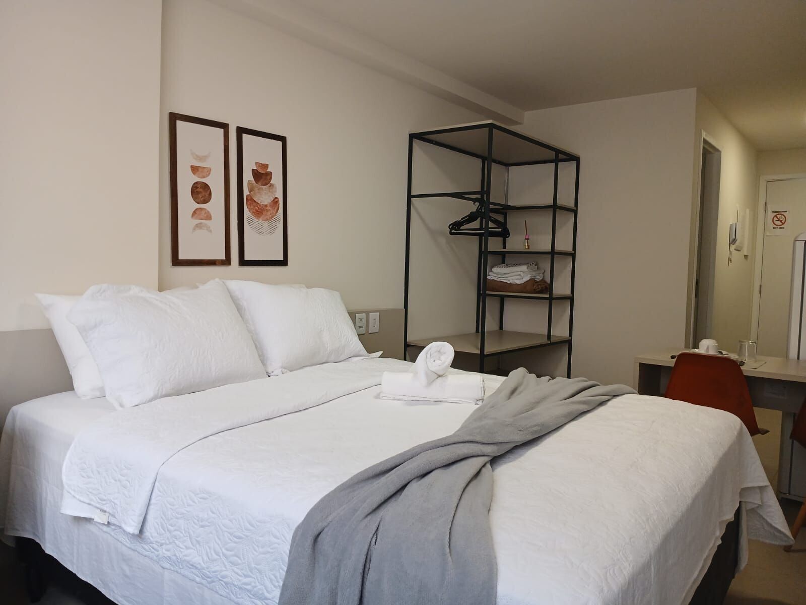 Une chambre d’hôtel comprenant un lit, un bureau, une chaise, une armoire et deux tableaux encadrés accrochés au mur.