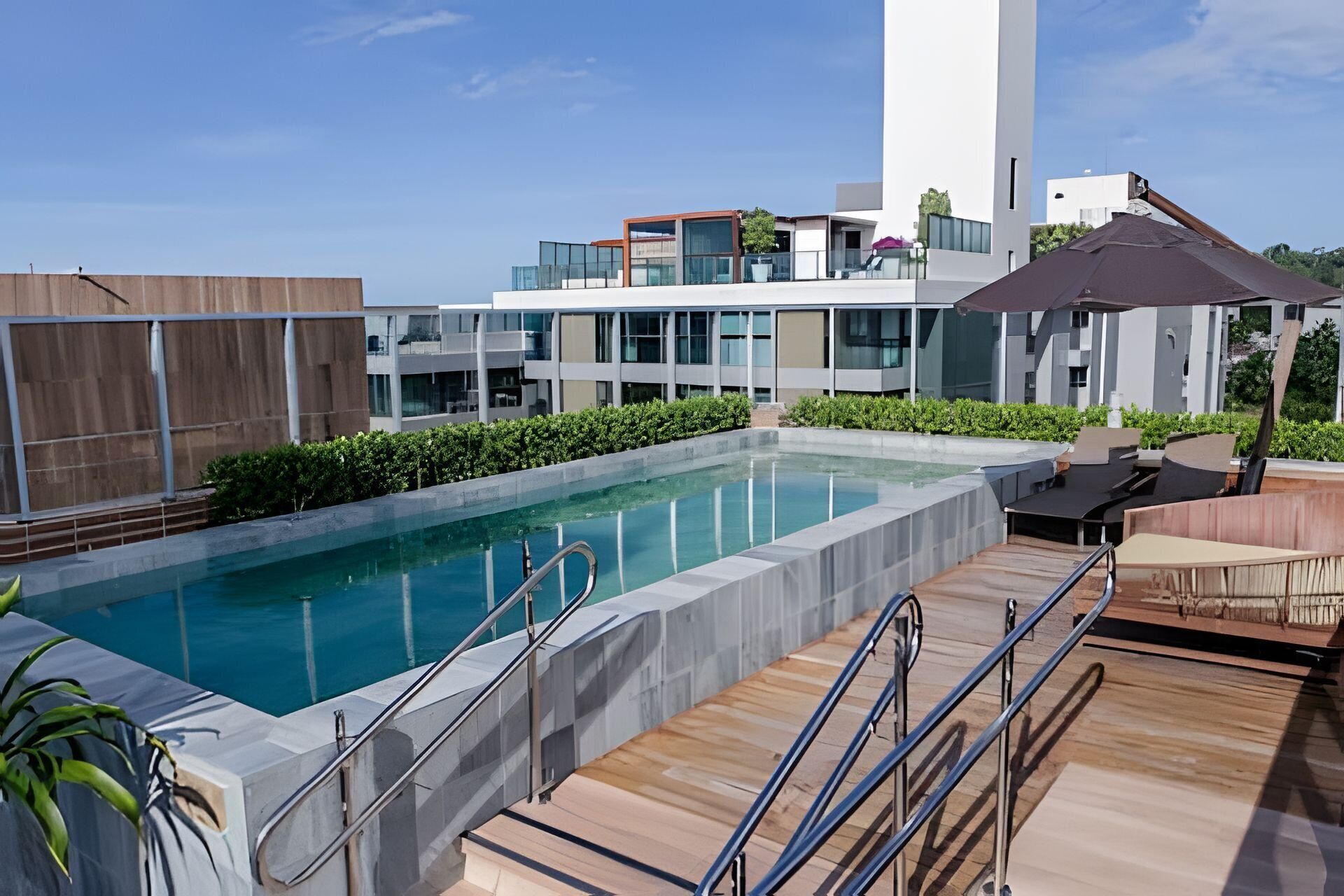 A modern outdoor pool area with a wooden deck, metal railings, and a view of contemporary buildings in the background.