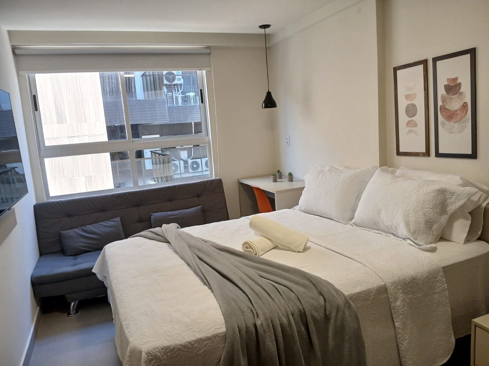 A bedroom with a bed, a sofa, a desk, and a window with a view of the outside.