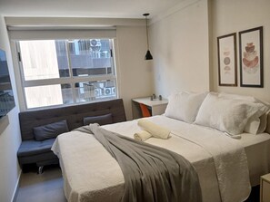 A bedroom with a bed, a sofa, a desk, and a window with a view of the outside. - Vivendas do Mar (João Pessoa)