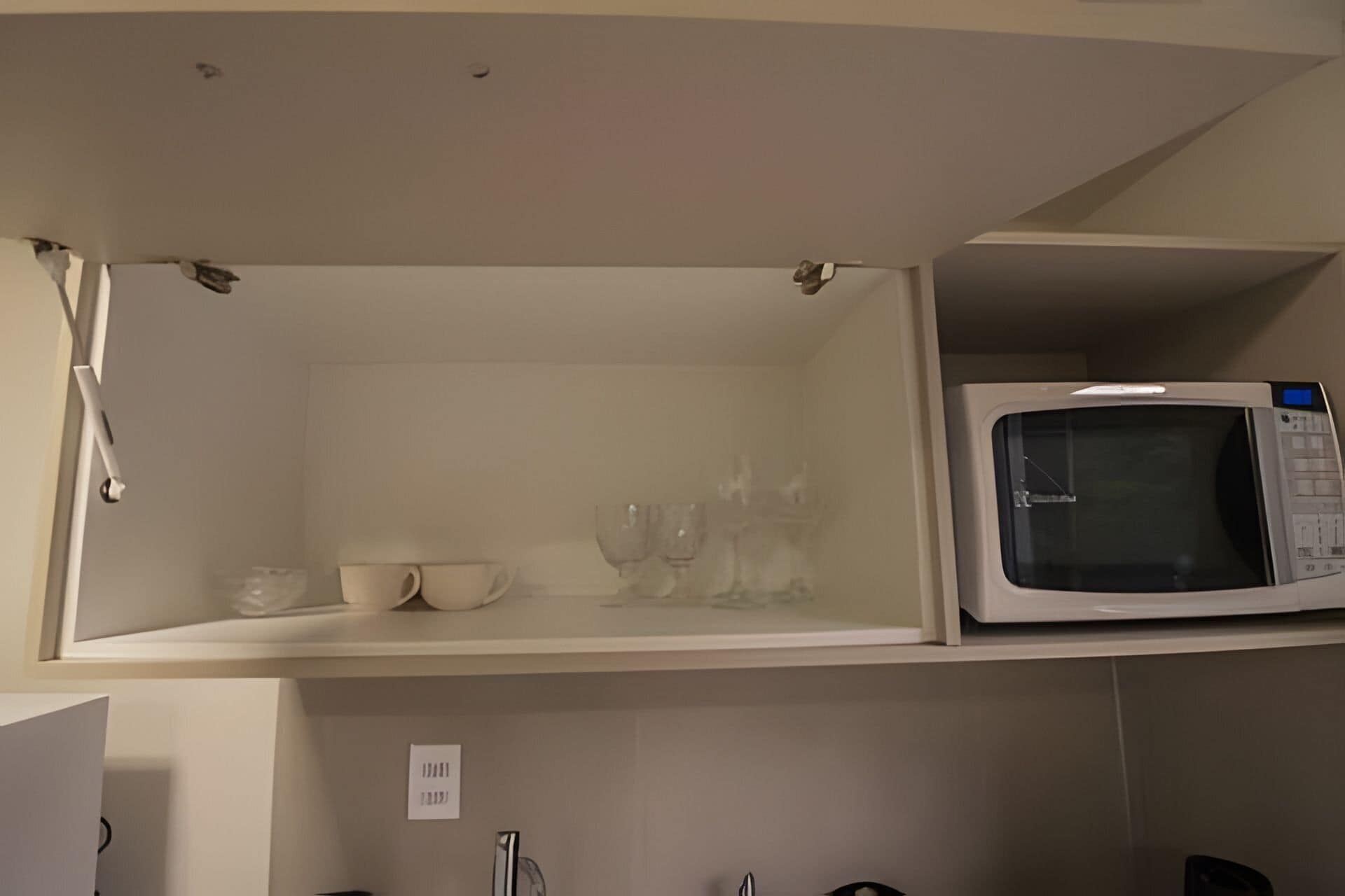 A kitchen with a microwave on the upper shelf and a cabinet below.