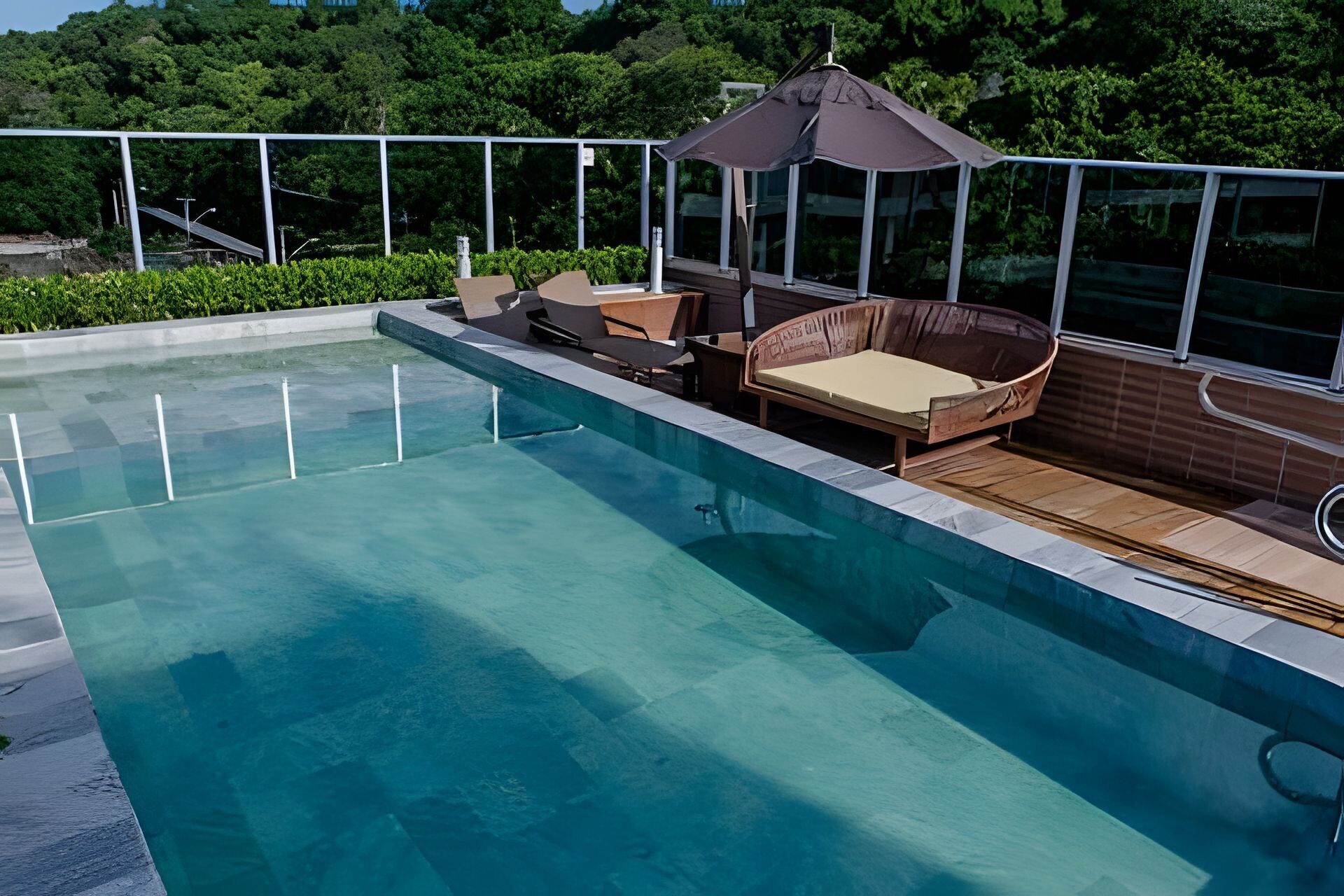 Piscina com deck de madeira, área de estar acolchoada e pérgola.