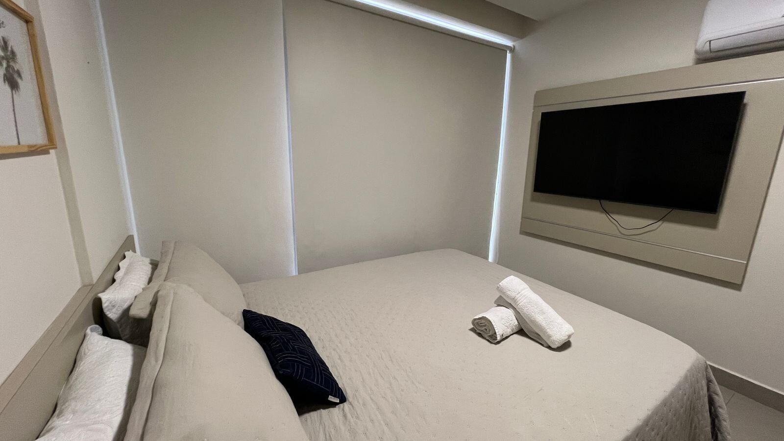 A hotel room with a bed, pillows, a TV, and a window.