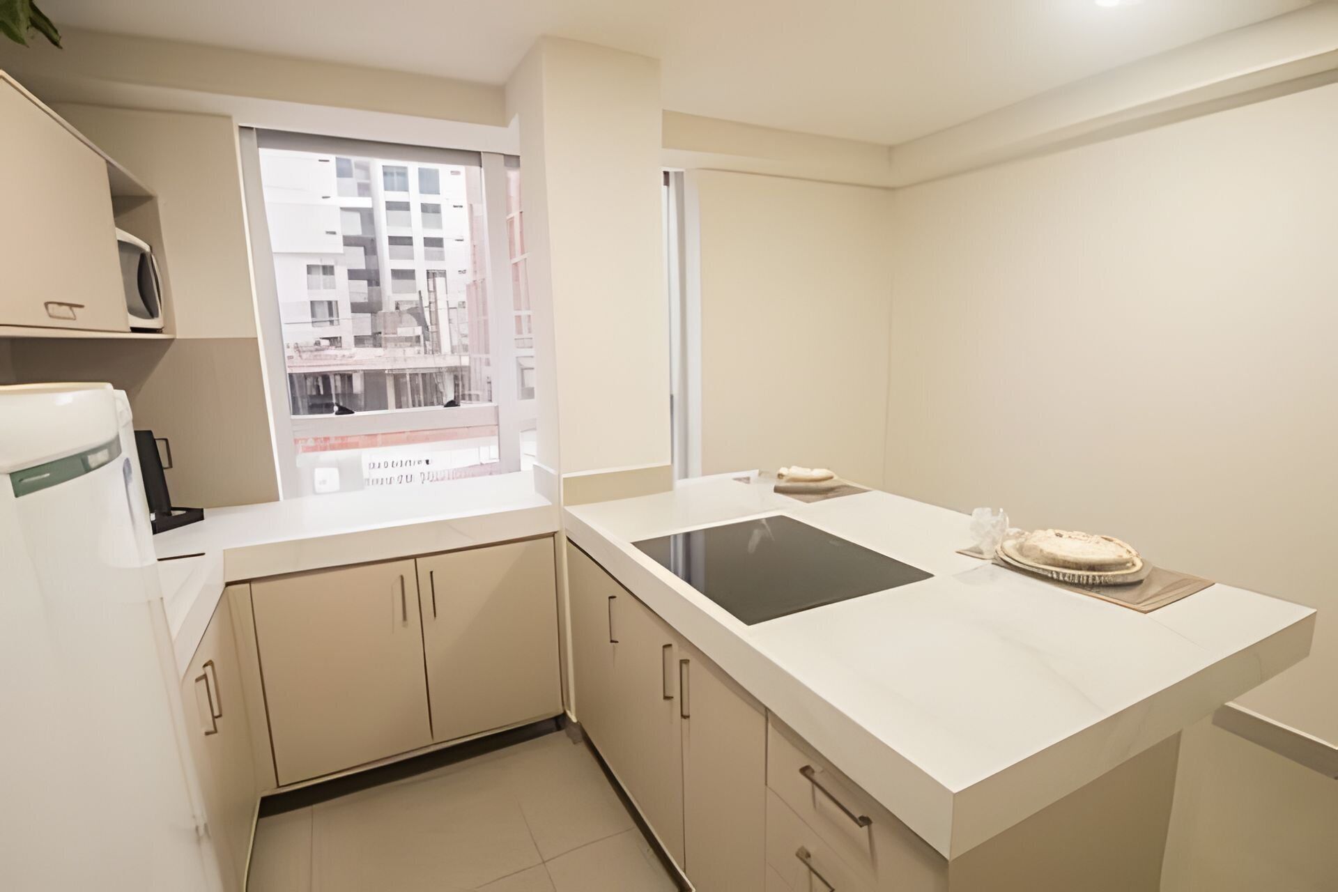 A modern kitchen with a built-in stove, a window with a view of buildings, and a small countertop with a cake.