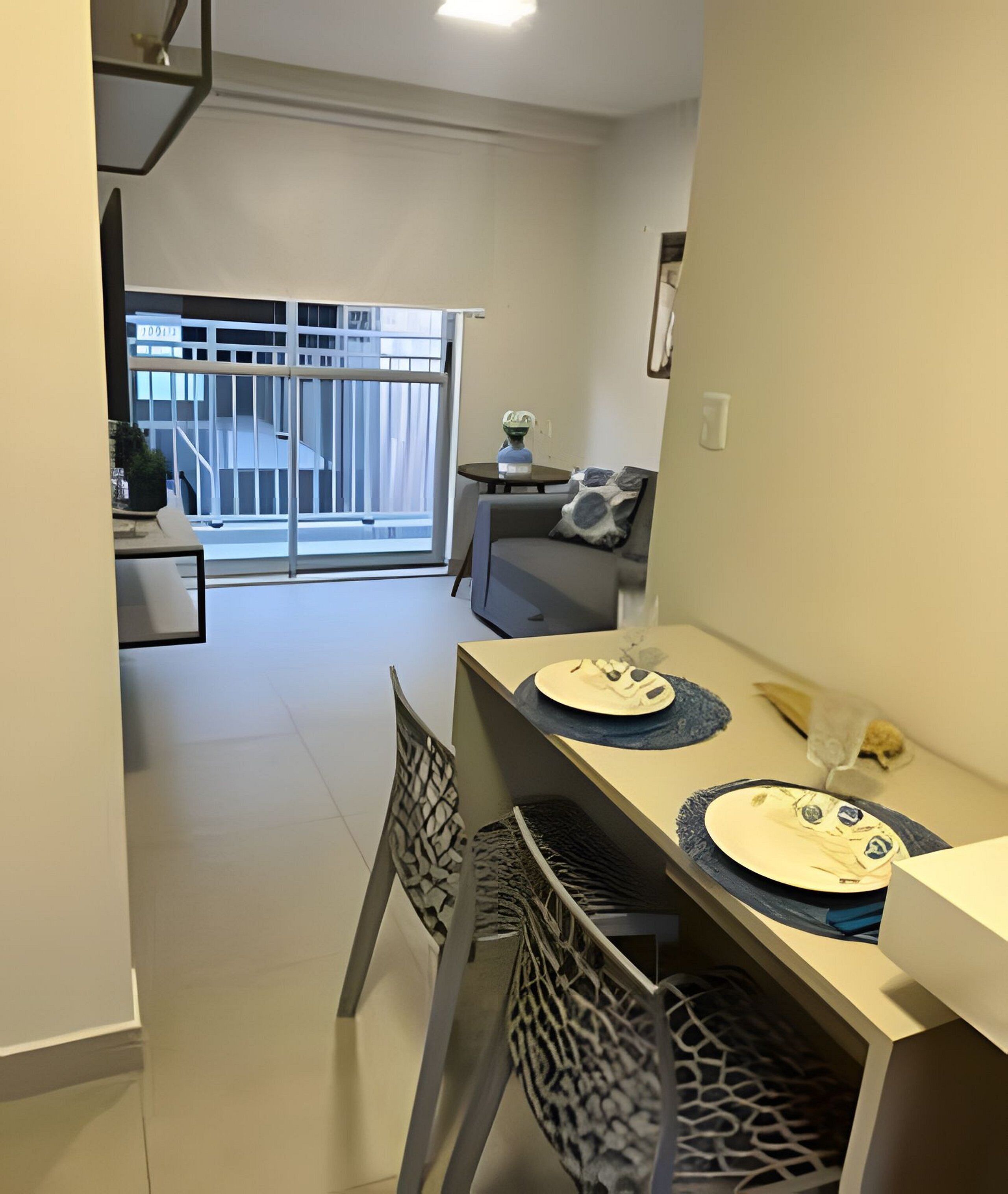 A dining area with a table set for two, a sofa, and a view of a building outside.