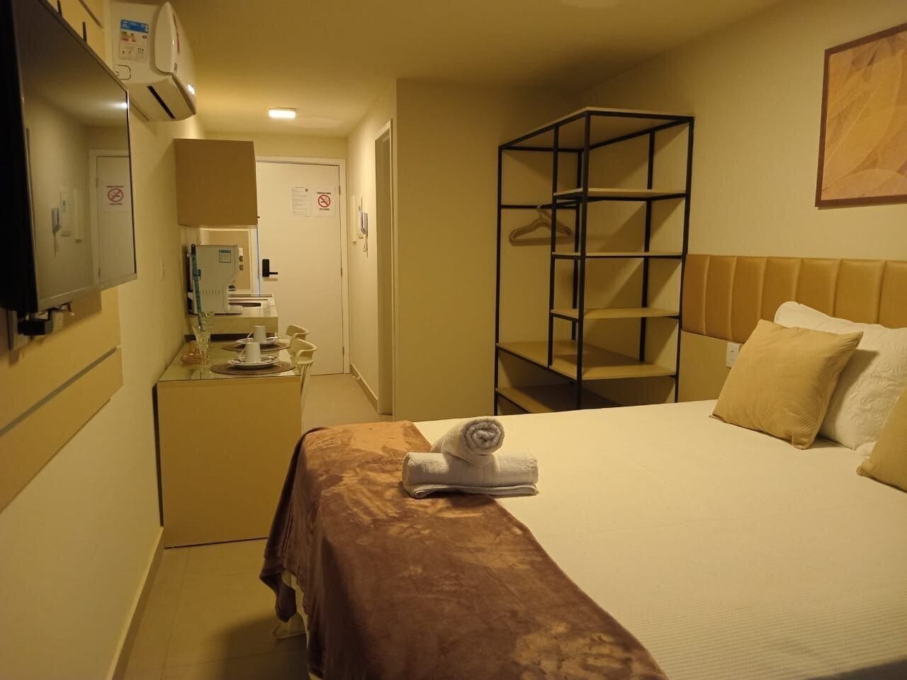 Hotellihuone, jossa on sänky, työpöytä tietokoneella, peili ja vaatekaappi.