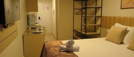 Une chambre d’hôtel comprenant un lit, un bureau avec un ordinateur, un miroir et une armoire.