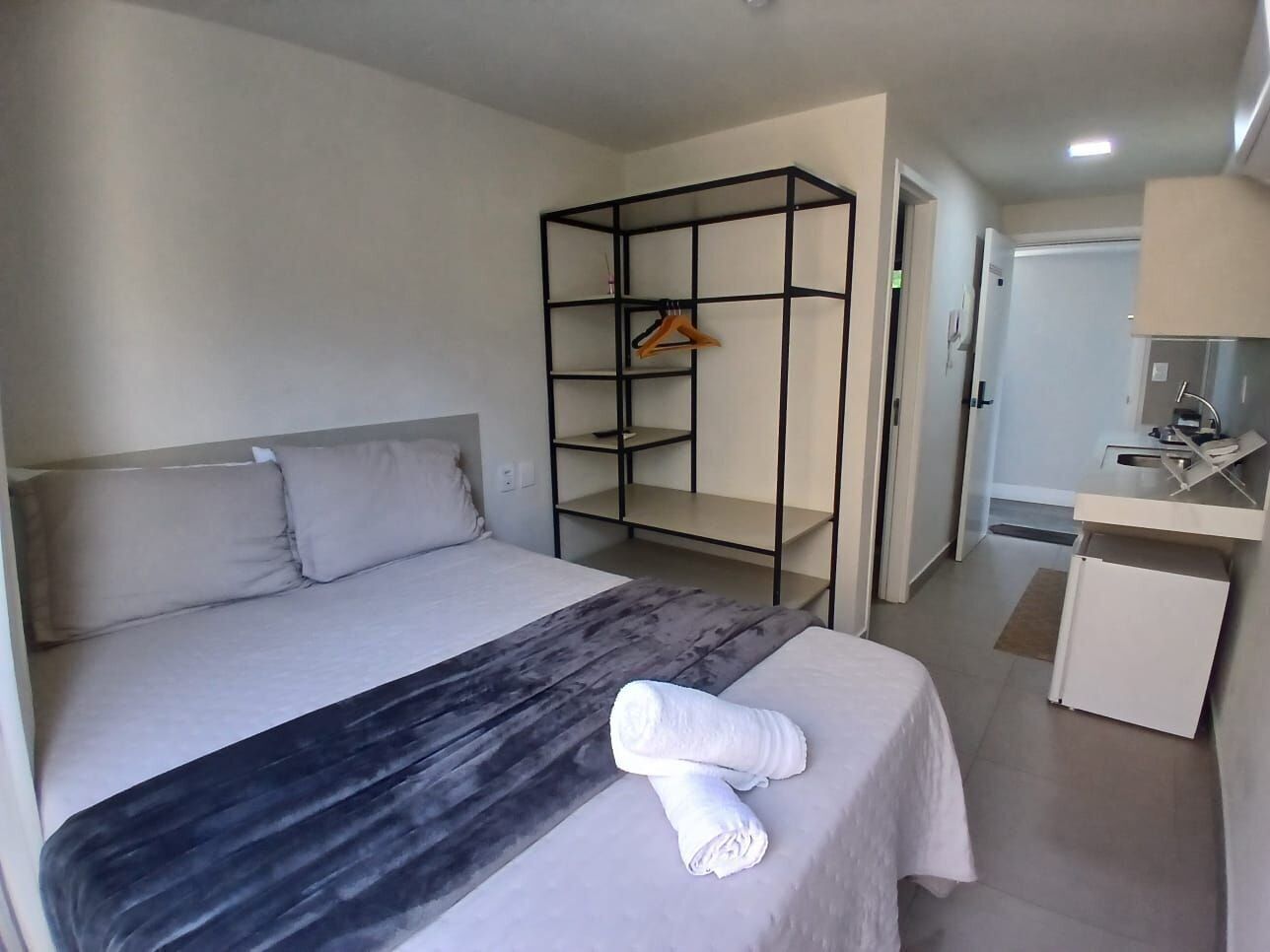 Una habitación de hotel con cama, un escritorio pequeño con espejo, un armario y una toalla sobre la cama.