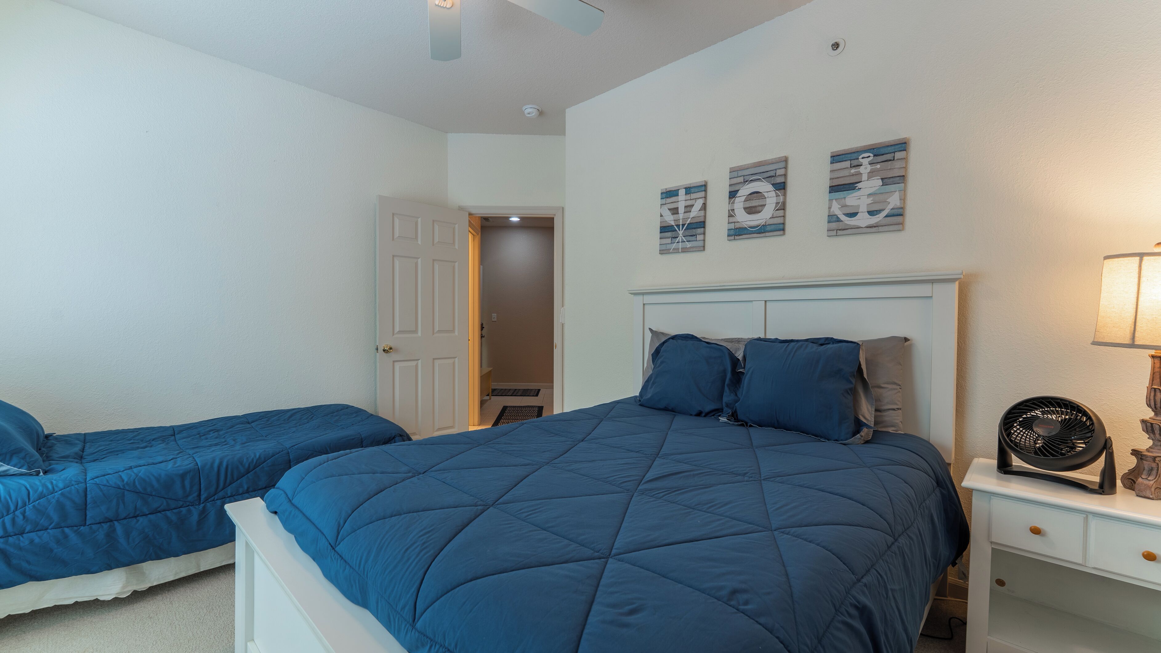 Quarto com duas camas, mesa de cabeceira, abajur e decoração na parede.