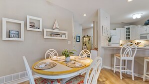 Un comedor con una mesa redonda, sillas blancas y una cocina al fondo.