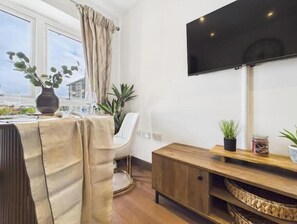 Una habitación con una mesa de comedor, sillas, un sofá, un televisor fijado a la pared y un armario de madera.
