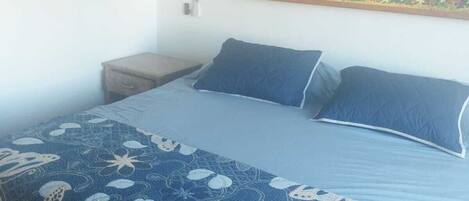 A bedroom with a bed, a nightstand, a wall-mounted painting, and a window.