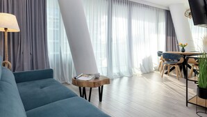 A modern living room with a sofa, a small wooden table, a flat-screen TV, and a dining area with chairs and a table. - Wavescape - Wave Resort & Spa (Międzyzdroje)
