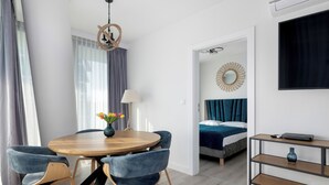 A modern room with a round wooden dining table, blue upholstered chairs, a lamp, a bed with a blue headboard, a TV, and a decorative mirror on the wall. - Wavescape - Wave Resort & Spa (Międzyzdroje)