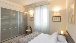 Camera d'albergo con un letto, una sedia, un armadio, una finestra con tende e luci a parete.