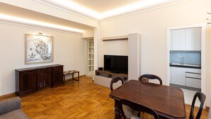 Un soggiorno moderno con pavimento in legno, un tavolo da pranzo, una televisione, un mobile contenitore e un angolo cottura.
