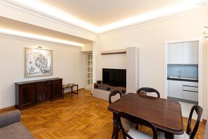 A modern living room with a wooden floor, a dining table, a TV, a cabinet, and a kitchen area. - Alberico II Apartment (Rome)