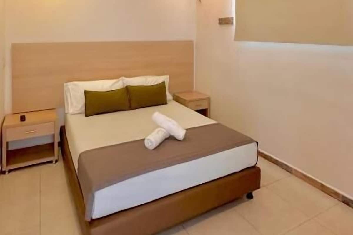 A hotel room with a bed, a nightstand, a wall-mounted TV, and a ceiling light.