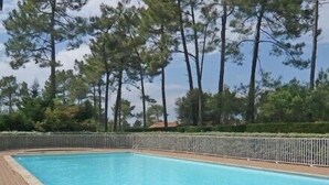 Une piscine rectangulaire avec un escalier en métal, entourée d’un chemin pavé en briques et d’une clôture en métal.