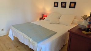 A neatly made bed with a blue blanket, a bedside table with a lamp, and three framed pictures on the wall.