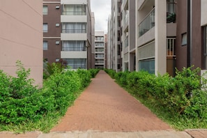 Un chemin bordé de verdure et flanqué de bâtiments modernes dotés de balcons et de fenêtres.