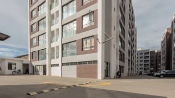 A multi-story residential building with a modern architectural design, featuring a mix of glass and concrete facades, and a paved ground with a yellow tactile paving strip.