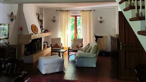 Uma sala de estar com lareira, sofá, mesa de jantar e escada.