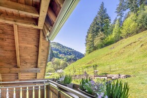 Un balcone in legno con vista su un pendio verde e alberi.