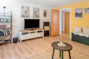 Ein Wohnzimmer mit Fernseher, Bücherregal und einer Couch.