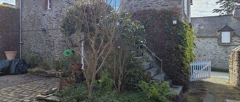 A stone building with a blue window, a small garden with a tree, and a white fence.