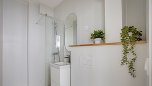 A modern bathroom with a glass shower enclosure, a white sink, and a wooden shelf with plants. - Quiet studio near Nation & Bois (Paris)