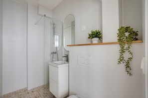 A modern bathroom with a glass shower enclosure, a white sink, and a wooden shelf with plants. - Quiet studio near Nation & Bois (Paris)