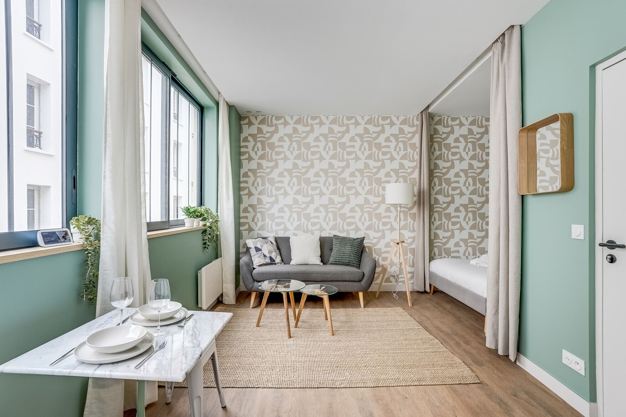 A room with a sofa, a small table with plates and glasses, a lamp, and a patterned wall.