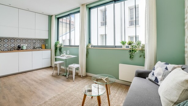 A modern kitchen with white cabinets, a small dining table with two chairs, and a glass coffee table. - Quiet studio near Nation & Bois (Paris)