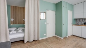 A room with a bed, a door, a mirror, and a kitchen area. - Quiet studio near Nation & Bois (Paris)
