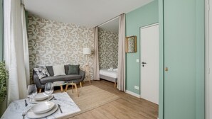 A room with a sofa, a dining table set for two, a bed, and a door. - Quiet studio near Nation & Bois (Paris)