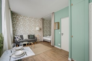 A room with a sofa, a dining table set for two, a bed, and a door. - Quiet studio near Nation & Bois (Paris)