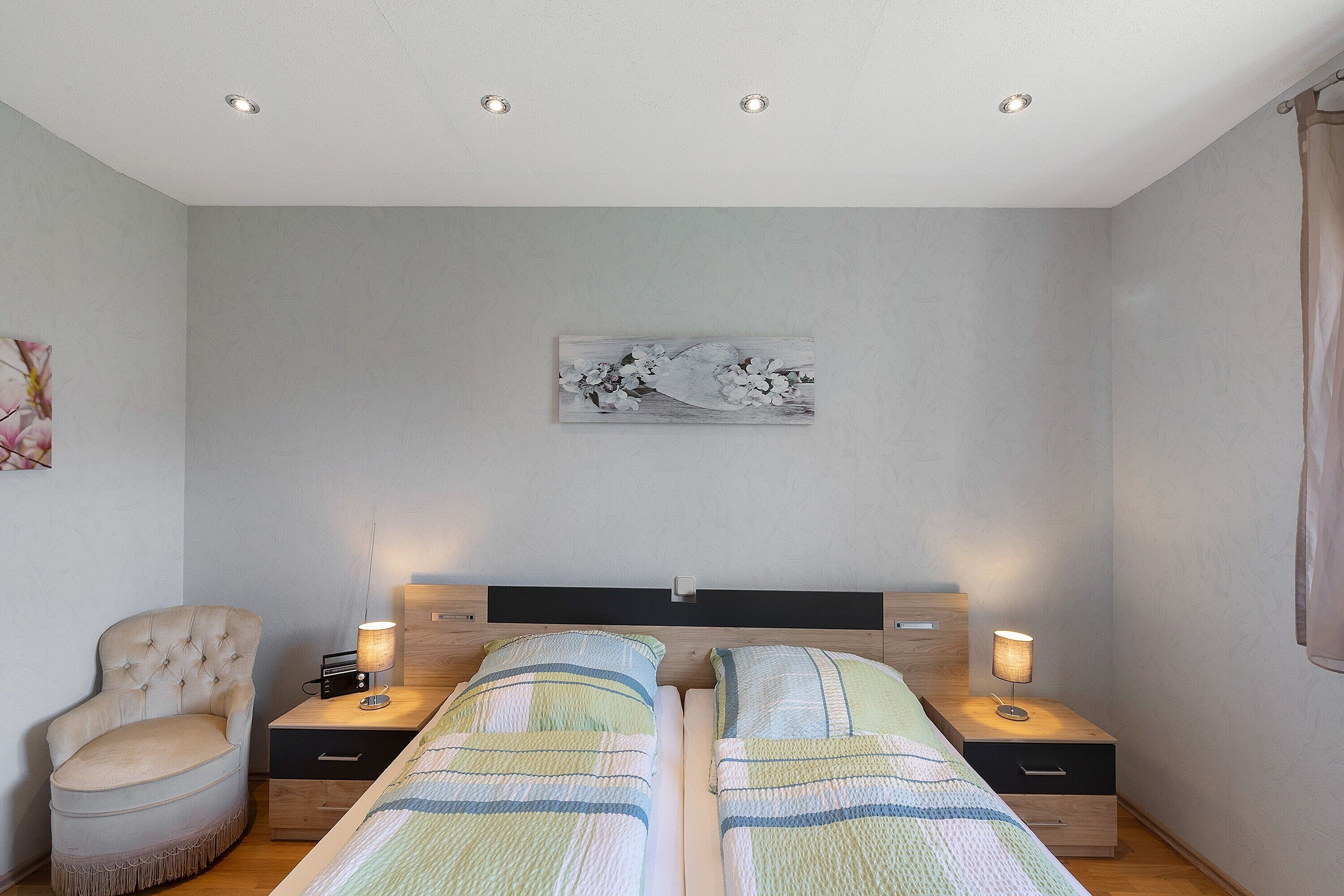 Camera da letto con due letti, una sedia, comodini, un quadro e luci a incasso nel soffitto.