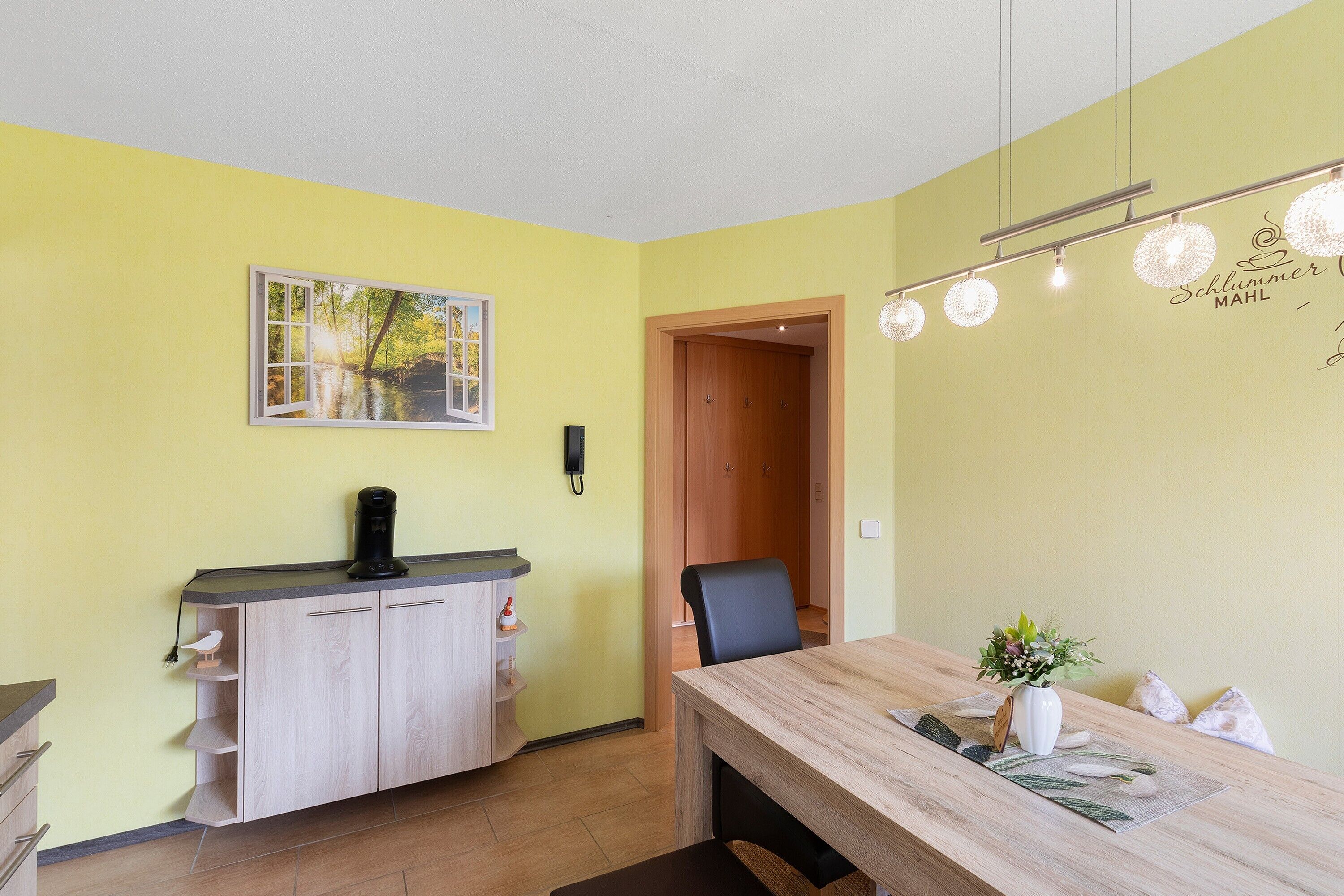 Una habitació amb un escriptori de fusta, una cadira, un armari amb prestatges, un quadre i una làmpada fixada a la paret.