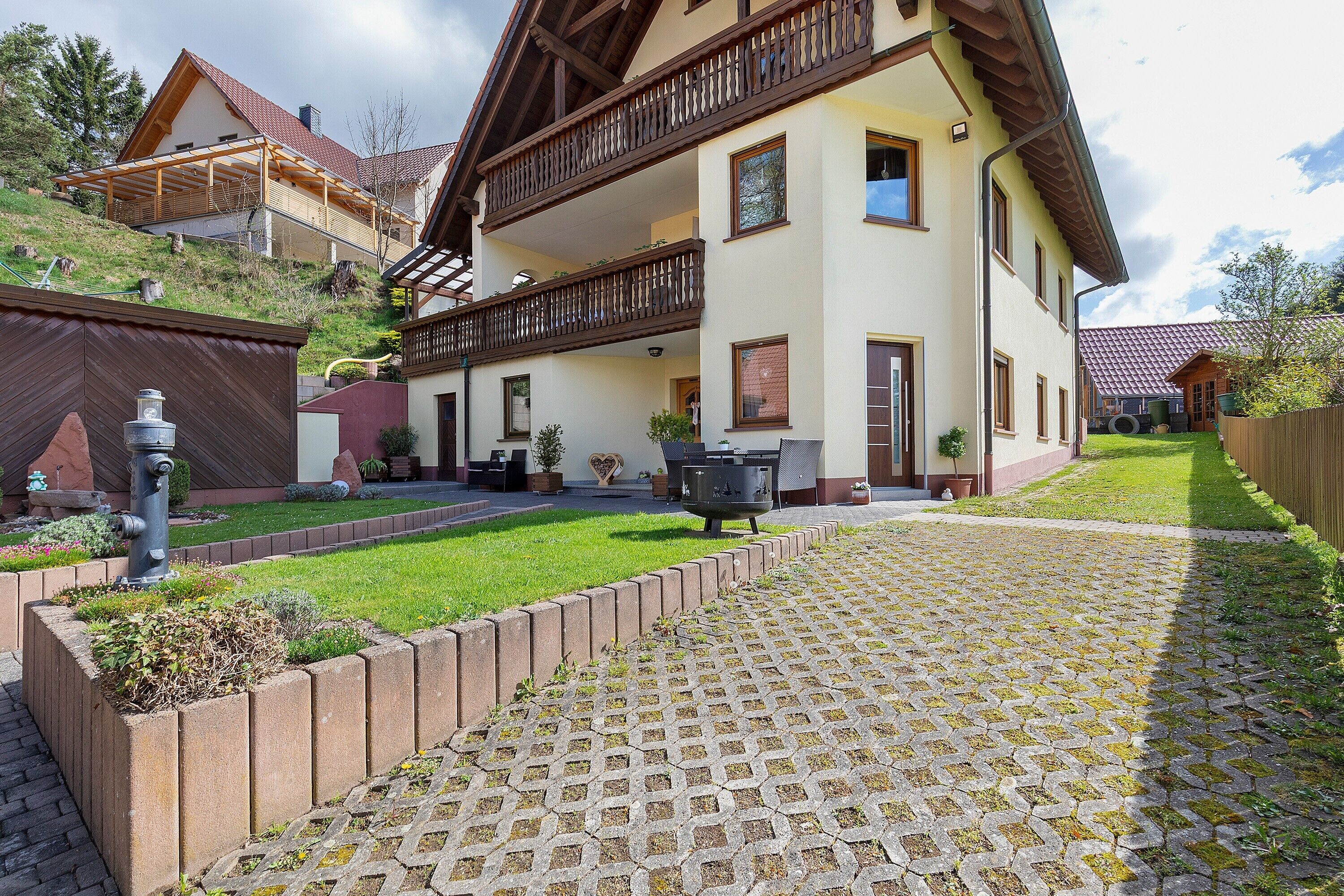 A two-story house with a balcony, a paved driveway, and a well-maintained lawn.
