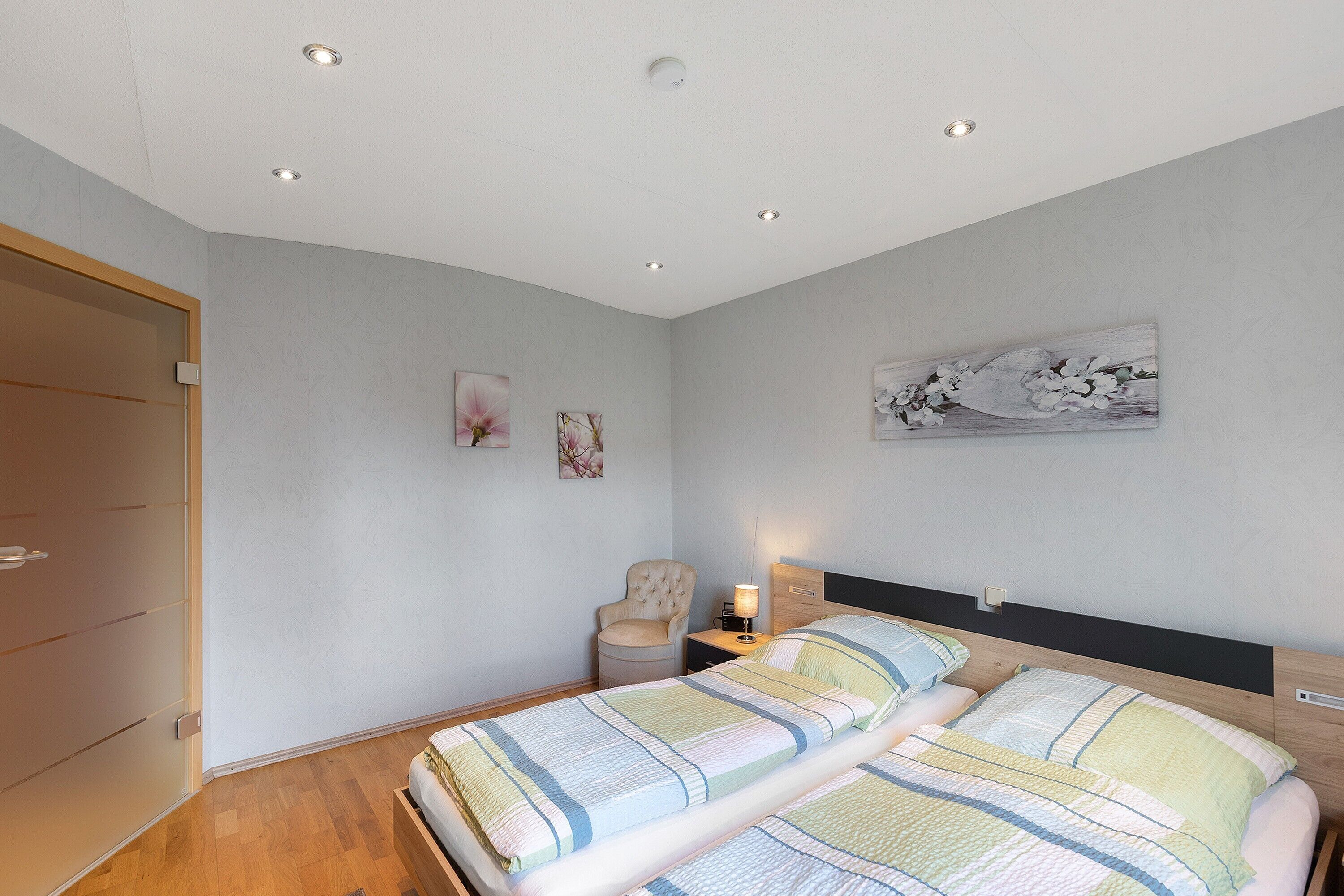 Ein Schlafzimmer mit zwei Betten, einem Sessel, einem Nachttisch mit Lampe und einem Bild an der Wand.