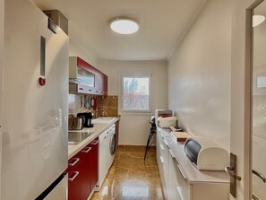 Eine kleine Küche mit Kühlschrank, Herd, Spüle und einem Fenster mit Blick auf Bäume.