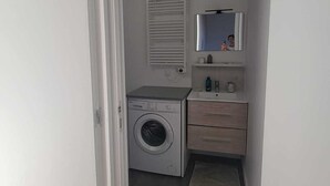 Ett tvättrum med en tvättmaskin, en handduksställning, en spegel och ett litet skåp.
