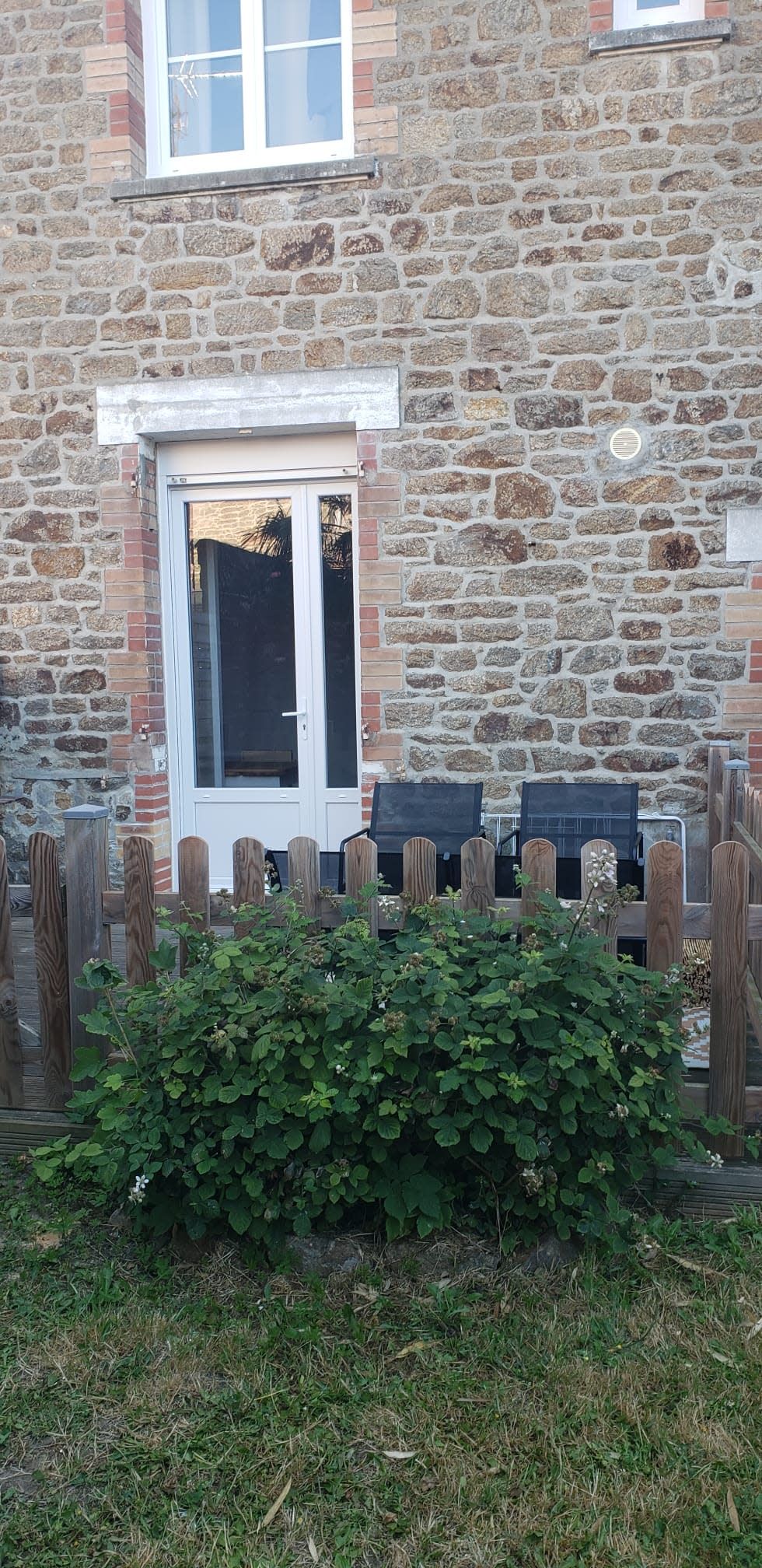 A stone building with a white door, wooden fence, and a bench.