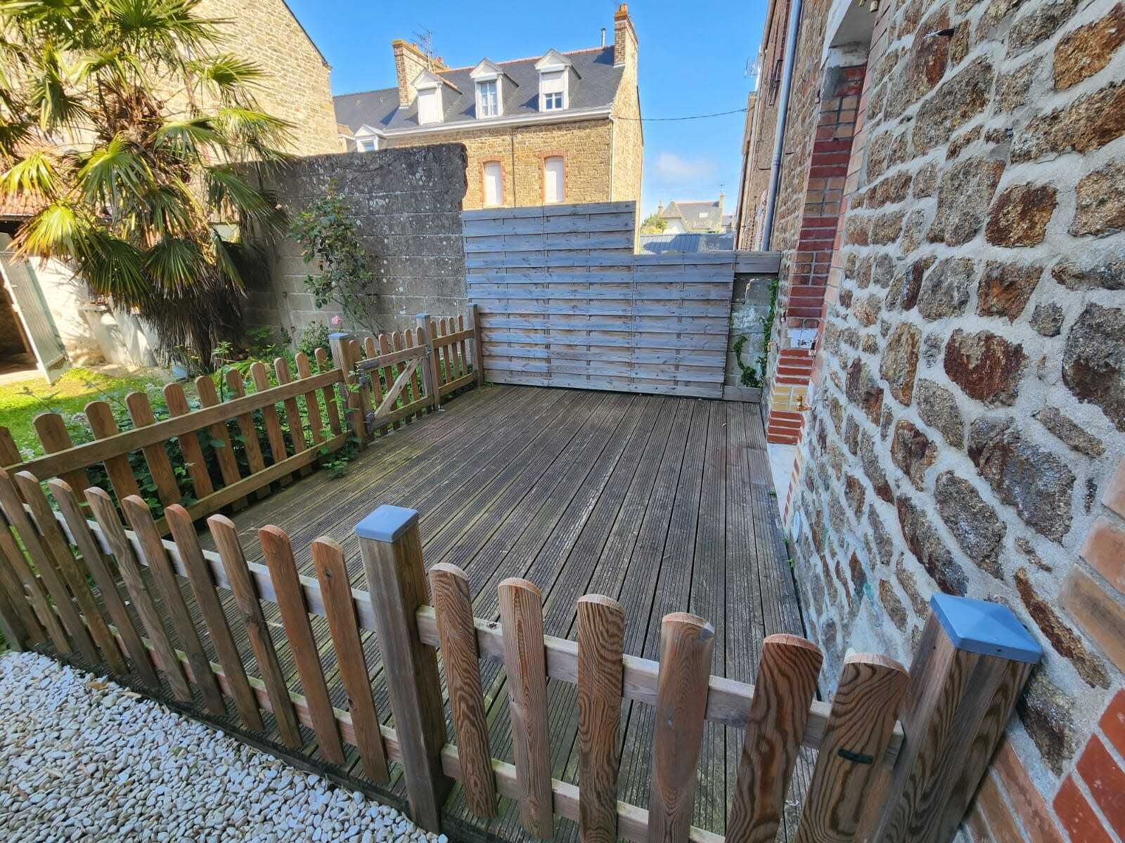 Eine Holzterrasse mit Holzzaun, einer Steinmauer und einem Gebäude im Hintergrund.