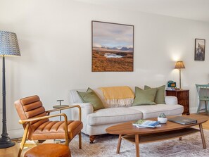 A living room with a sofa, armchair, coffee table, and a painting on the wall. - The Old Forge Clifden (Clifden)